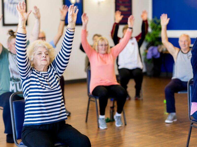 Men and women in chairs with arms raised doing exercises
